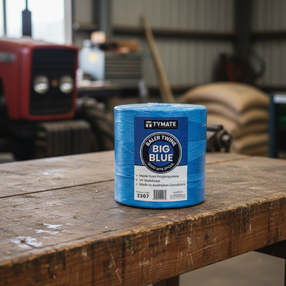 Baler twine spool TYMATE BALER TWINE BIG BLUE 8000 MTR SPOOL on wooden workbench in farm workshop with tractor in background. Text: "TYMATE BALER TWINE BIG BLUE 8000 MTR SPOOL Made from Polypropylene UV Stabilised Made to Australian Conditions 2307"
